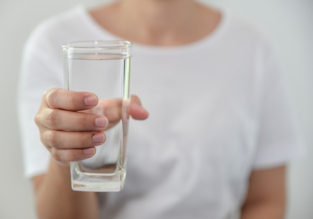 Young woman holding drinking water glass in her hand. Healthy drink and healthcare concept.