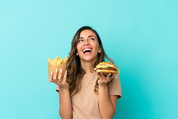 Young woman holding fried chips  and burger over isolated background