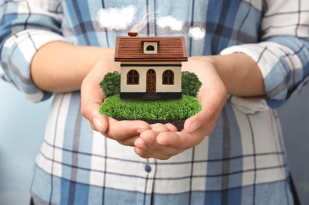 Young woman holding her dream house with beautiful green lawn closeup