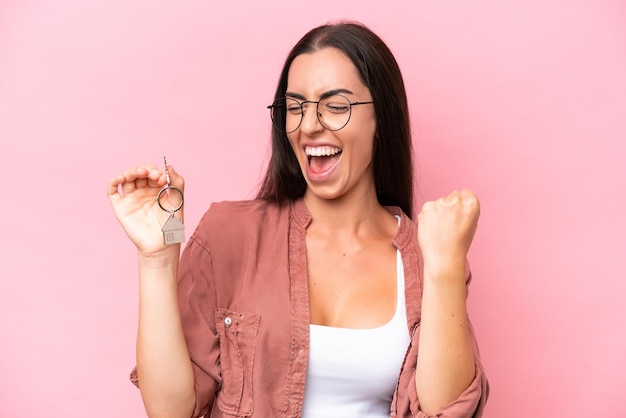 Young woman holding home keys isolated on pink background celebrating a victory