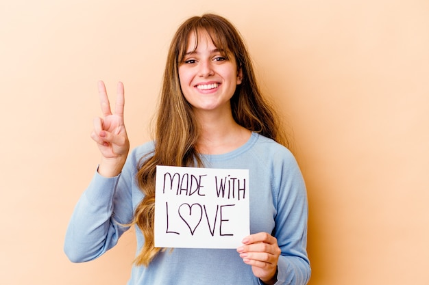 Young woman holding a made with love placard isolated showing number two with fingers