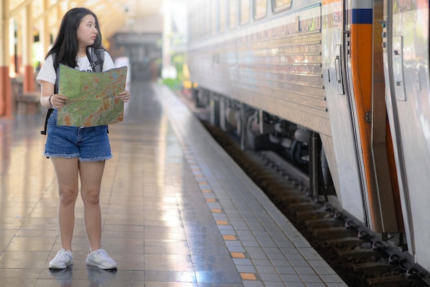 A young woman holding a map standing on the platform looking at the train