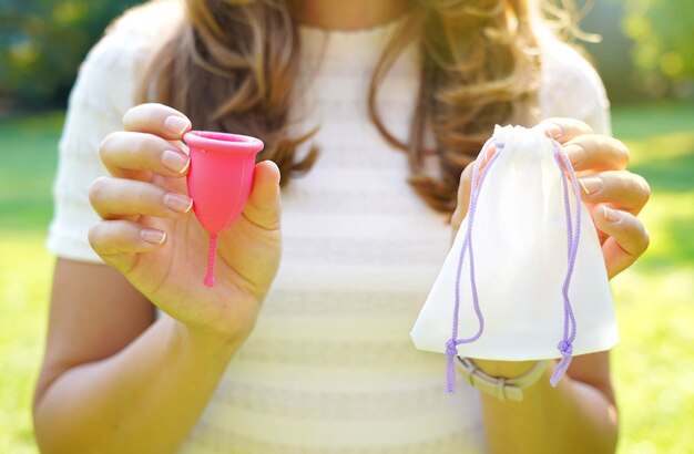 Young woman holding a menstrual cup with bag standing against green natural background