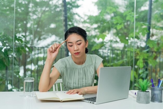 Young woman holding pencil thinking and planning business strategy while sitting at office desk