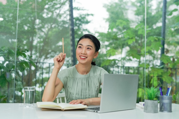 Young woman holding pencil thinking and planning business strategy while sitting at office desk