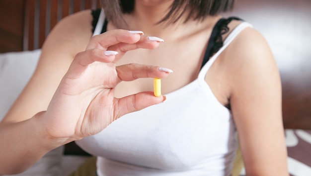 Young woman holding pill on bedroom.