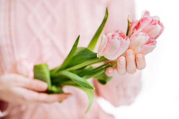 Young woman holding pink tulips on a white background. Blur portrait, closeup, copy space, selective focus.