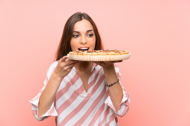 Photo young woman holding a pizza over isolated pink wall