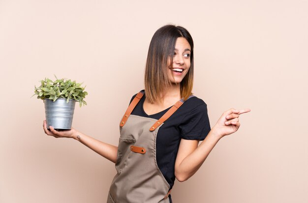 Young woman holding a plant pointing to the side to present a product