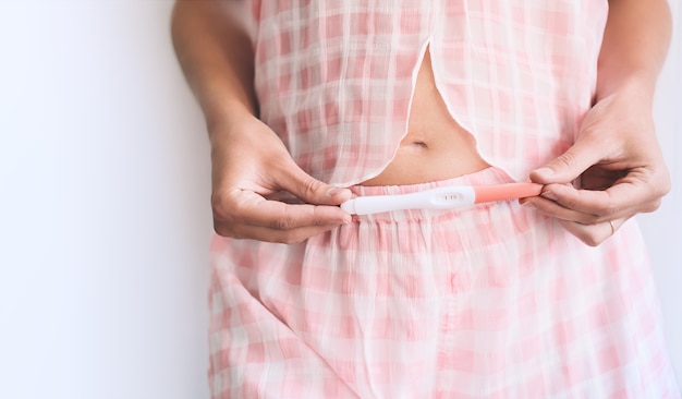 Young woman holding pregnancy test in hands and hugging her belly