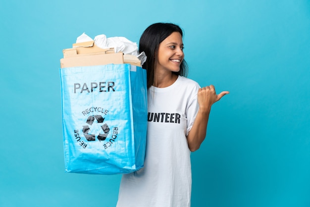 Young woman holding a recycling bag full of paper pointing to the side to present a product