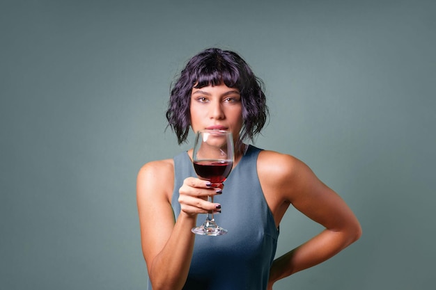 Young woman holding a red wine glass watching the camera Isolated on a clean background People drinking wine concept