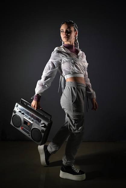 Young woman holding a retro tape recorder with one hand and looking away in studio shot