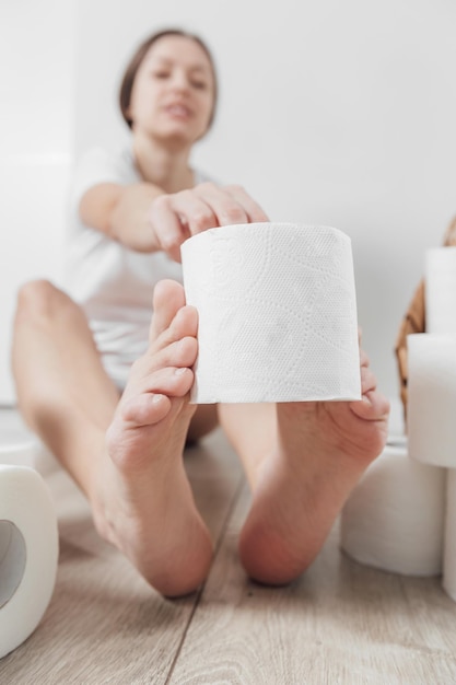 Young woman holding roll of toilet paper by foots