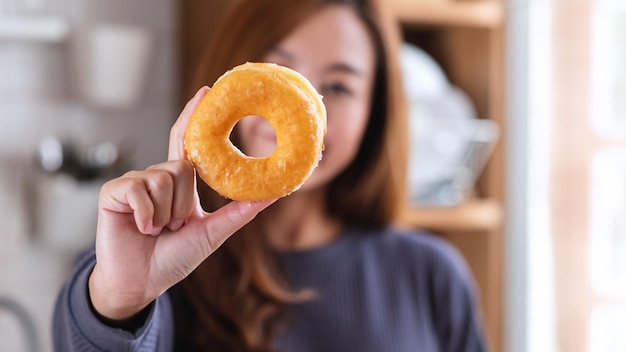 A young woman holding and showing a piece of glazed donut at home