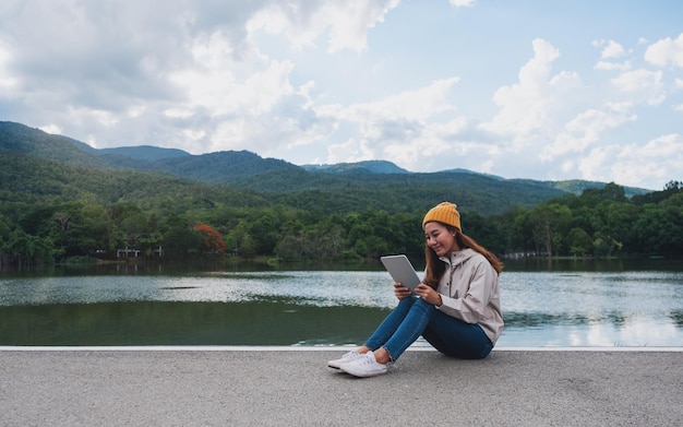 A young woman holding and using digital tablet while traveling mountains and lake