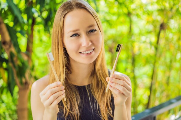 Young woman holds a bamboo toothbrush on a background of green growing bamboo