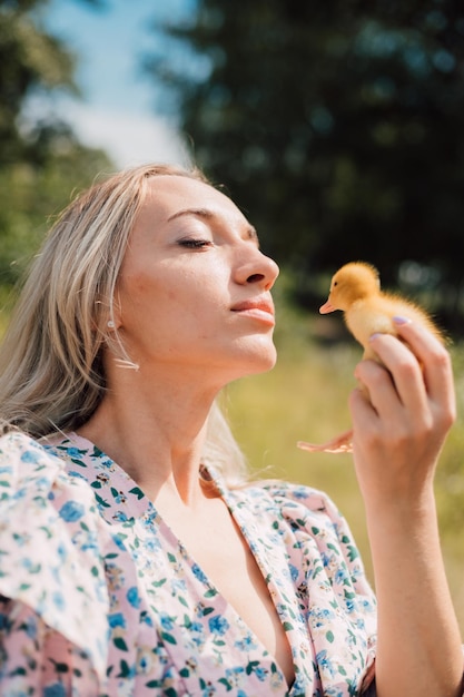 A young woman holds a duckling in her hands and closes her eyes enjoying