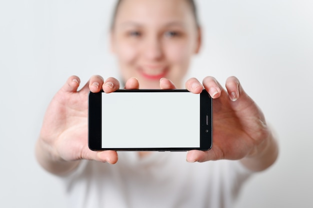 A young woman holds the phone horizontally with a white screen with a place for copyspace.