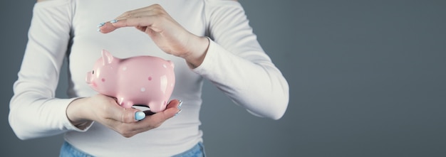 A young woman holds a piggy bank in her hand. Concept of saving money or savings. against a gray scene