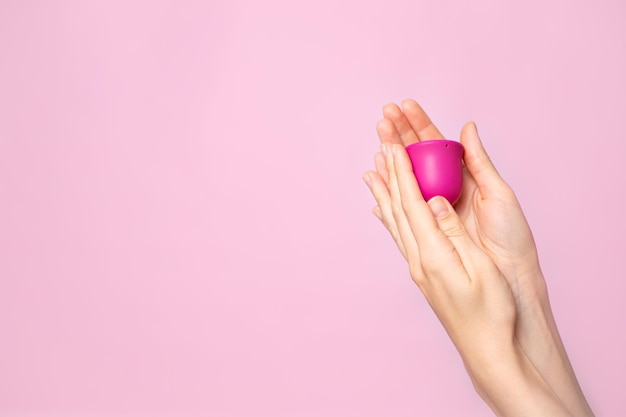 A young woman holds a pink menstrual cup in her hand Pink colored background Space for text Ecofriendly silicone women39s health cycle High quality photo