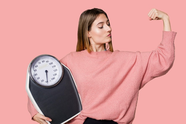 A young woman holds a scale feeling happy and motivated by her healthy diet and exercise change