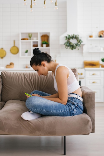 Young woman holds a smartphone in her hands hunched over sitting on the couch