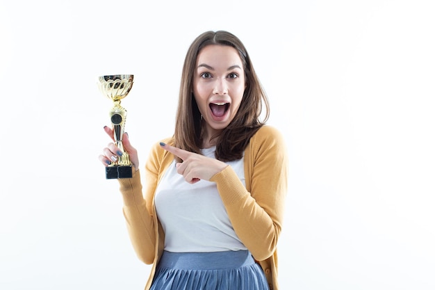 A young woman holds the winner's gold cup on a white background Emotional portrait of the model