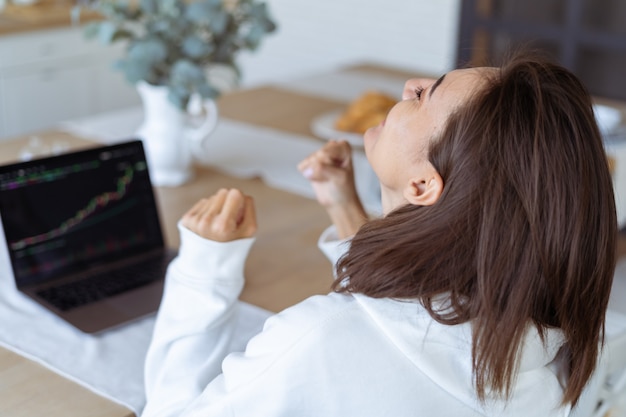 Young woman at home in the kitchen in a white hoodie with a laptop, a graph of growth on the screen