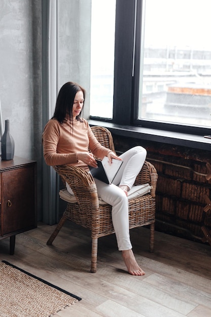 Young woman at home sitting on chair relaxing in her living room reading book