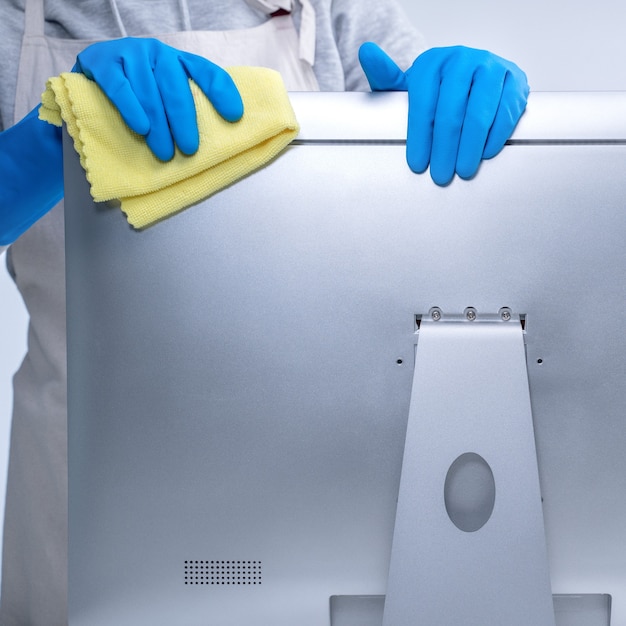 Young woman housekeeper in apron is cleaning silver computer surface with blue gloves, wet yellow rag, close up, copy space, blank design concept.