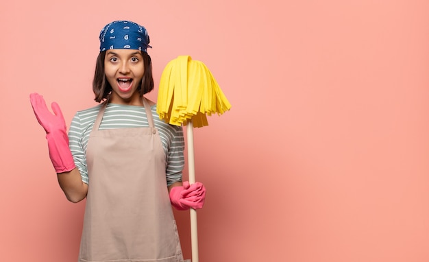 Photo young woman housekeeper feeling happy, excited, surprised or shocked, smiling and astonished at something unbelievable