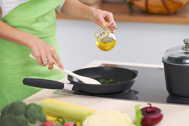 Young woman housewife cooking in the kitchen while adding olive oil Concept of fresh and healthy meal at home