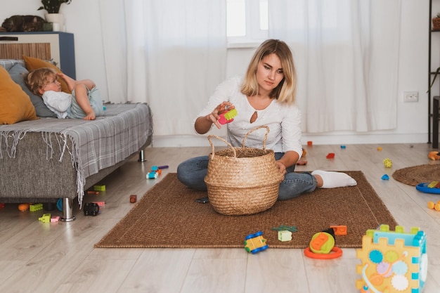 Young woman housewife puts toys in the basket with her little son at home