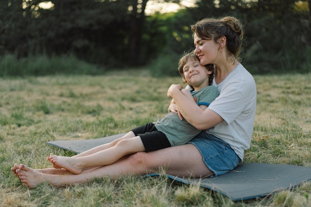 Young woman hugging her little son at sunny in the meadow