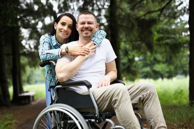 Young woman hugs disabled man in wheelchair on walk in park