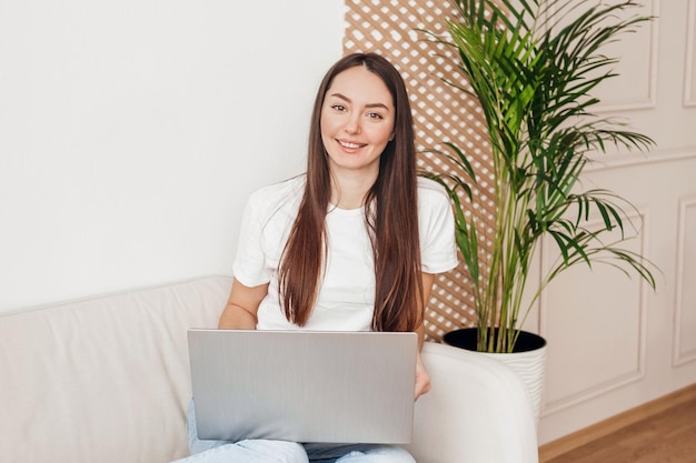 Young woman interior designer is sitting on the sofa with a laptop looking at the camera