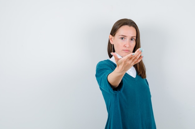 Young woman inviting to come in sweater over white shirt and looking confident , front view.