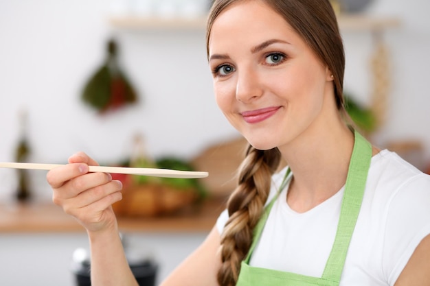 Young woman is cooking in a kitchen Housewife is tasting the soup by wooden spoon