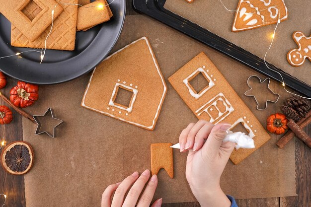 Photo young woman is decorating christmas gingerbread house cookies biscuit at home with frosting topping in icing bag close up lifestyle