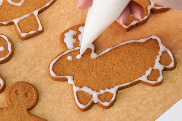 Young woman is decorating Christmas Gingerbread House cookies biscuit at home with frosting topping in icing bag close up lifestyle