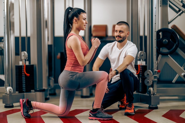 Young woman is doing training for legs with personal trainer in the gym.