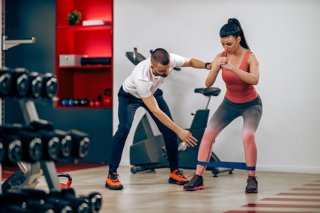 Young woman is doing training for legs with personal trainer in the gym.