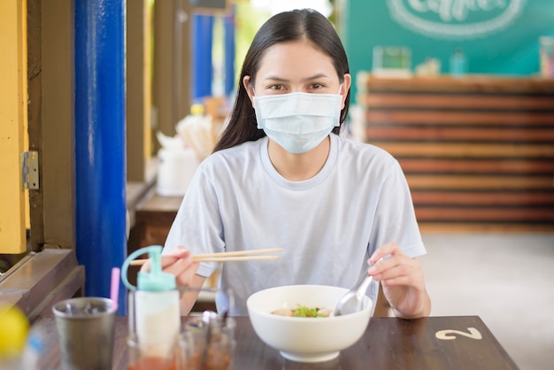 A young woman is eating Thai Street food , wearing face mask, New normal eating concept