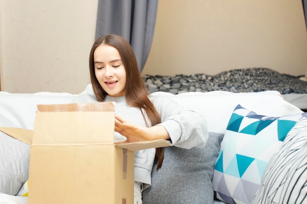 A young woman is happy to receive a parcel from an online store opens the box at home