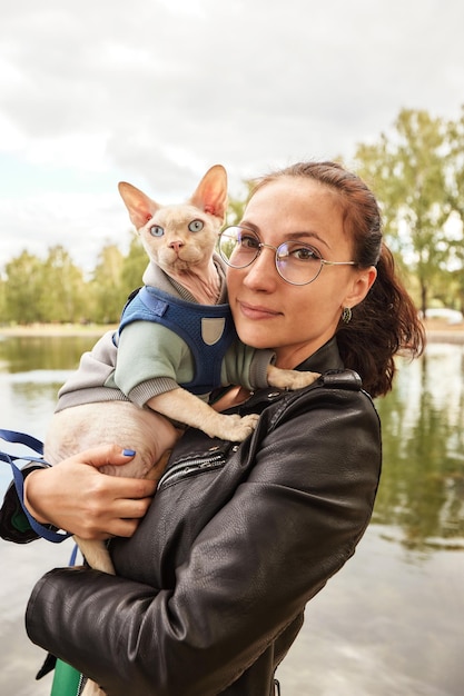 The young woman is holding her cat in amoveralls on her feet Cat on a walk Love to the animals Closeup