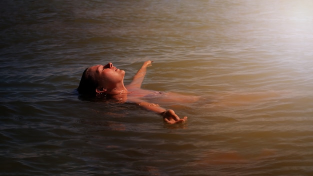 A young woman is immersed in water, the setting sun illuminates her.