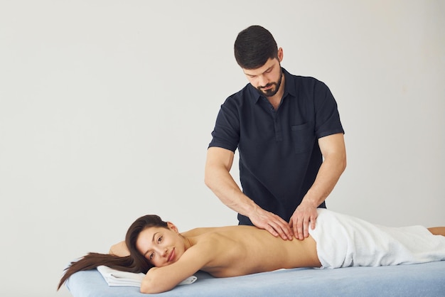 Young woman is lying down when man doing massage of her back at spa