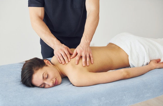 Young woman is lying down when man doing massage of her back at spa