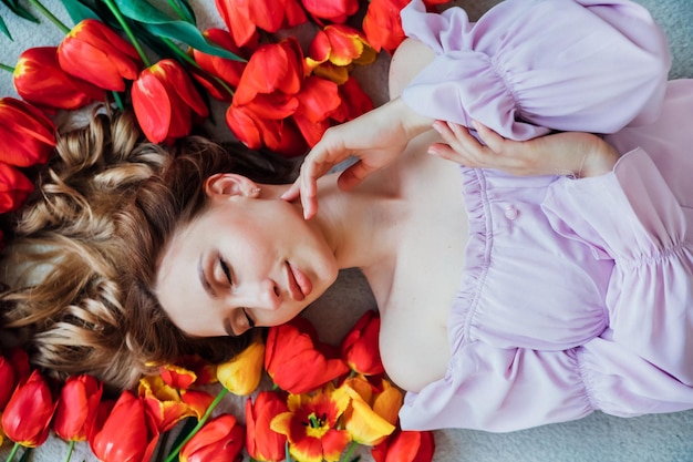 A young woman is lying on the floor among red tulips The concept of March 8 Valentine's Day Spring portrait of a woman